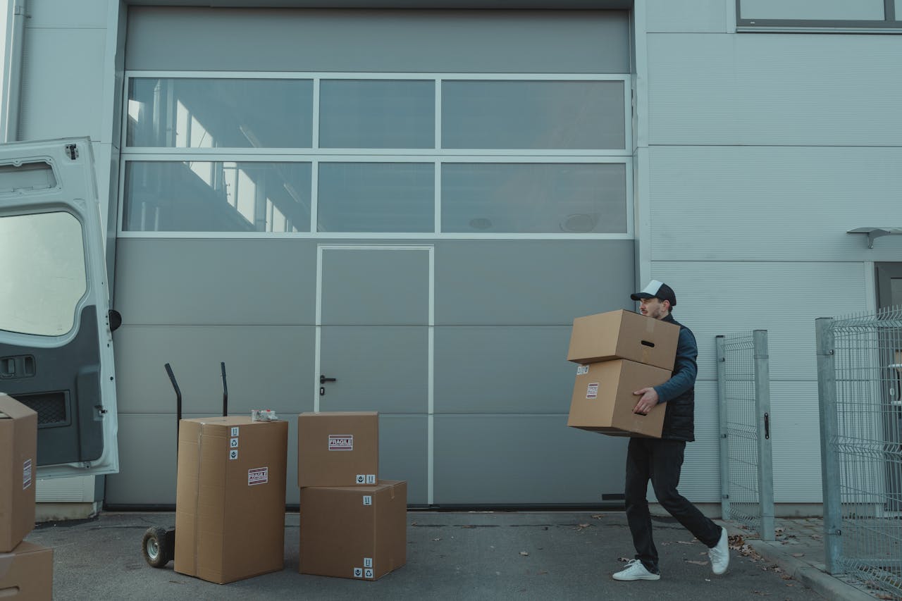 A delivery person carrying cardboard boxes outside a warehouse facility.